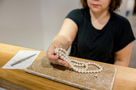 Photo for Crop of unrecognizable woman holding white pearl necklace in hand, small business owner, jewelry atelier, business concept - Royalty Free Image