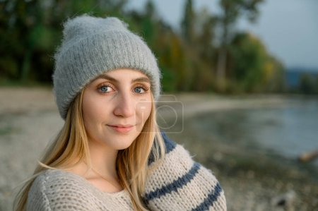 Foto de Vista lateral de la mujer joven en suéter cálido y acogedor y sombrero, respira aire limpio, mira al cielo con una sonrisa y ojos cerrados, camina con placer en el bosque de otoño. contenido sanitario de las personas - Imagen libre de derechos