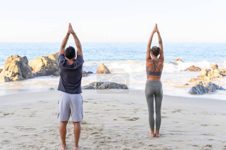 Téléchargez les photos : Vue de dos de la femme méconnaissable en vêtements de sport debout sur la plage de sable avec les bras levés tout en pratiquant le yoga le jour ensoleillé - en image libre de droit