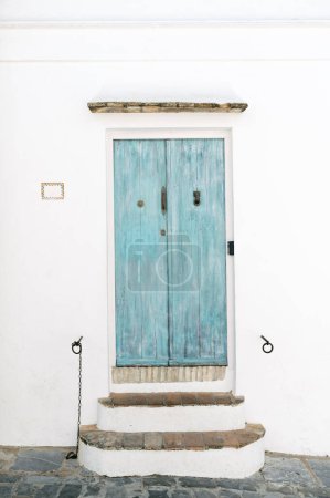 Foto de Una puerta de color turquesa envejecida, azul, colocada contra una pared blanca con escalones rústicos, que encarna el encanto de Andalucía - Imagen libre de derechos
