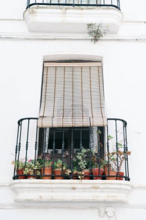 Foto de Edificio blanco con balcón de flores con protección solar tradicional frente a la ventana, macetas en un balcón en el sur de España, Andalucía, Viajes y concepto de vacaciones - Imagen libre de derechos