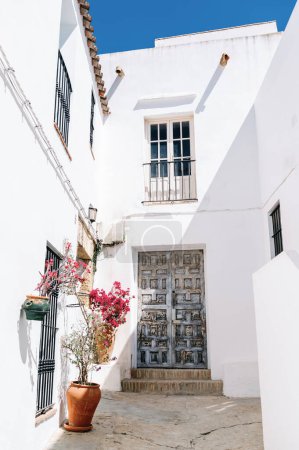 Téléchargez les photos : Bougainvilliers rose vif encadre une porte rustique en bois d'une maison traditionnelle espagnole blanche sous un ciel bleu clair, sud de l'Espagne, Andalousie, Vejer de la Frontera, Cadix, concept de voyage - en image libre de droit