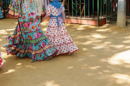 Téléchargez les photos : Robe de mode flamenco pleine de fleurs et de points de couleur, femme andalouse avec fille en costumes traditionnels costumes tziganes marchant à travers la Foire d'avril, Foire de Séville, Andalousie, Espagne. - en image libre de droit