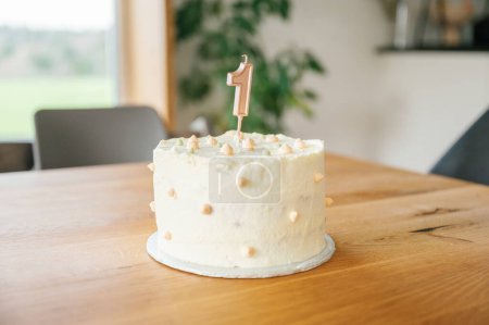 Photo for A simple yet elegant first birthday cake with a numeral one topper and a single candle on a wooden table - Royalty Free Image