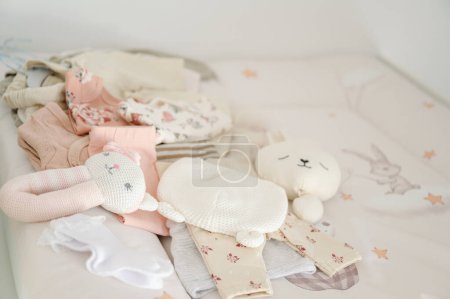 Still life photo of new baby clothes and toys on a bed