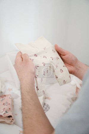 Photo for Vertical close-up photo of the hands of a man holding baby clothes - Royalty Free Image