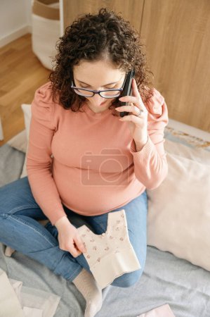 Téléchargez les photos : Vue de dessus verticale d'une femme enceinte adulte caucasienne parlant au téléphone portable dans la chambre - en image libre de droit