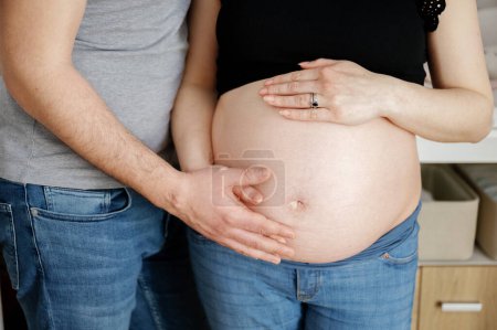 Photo for Part of an unrecognizable man touching the belly of his pregnant woman, couple wearing jeans and t-shirt. childbirth and pregnancy concept - Royalty Free Image