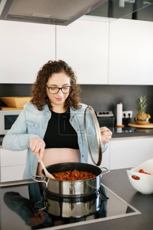 Photo for Vertical photo of a caucasian adult pregnant woman preparing home made food lunch alone in a modern kitchen at home. family concept - Royalty Free Image