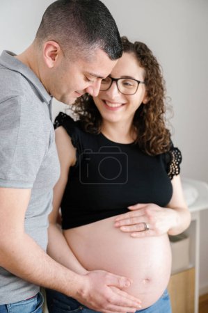 Téléchargez les photos : Portrait vertical en gros plan d'un couple enceinte romantique attendant le bébé, debout dans la crèche, homme touchant le ventre de sa femme, femme souriante, maternité, concept de parent - en image libre de droit