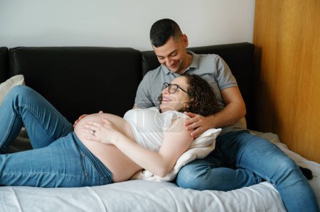 Téléchargez les photos : Femme enceinte allongée sur les genoux de son mari sur le canapé à la maison - en image libre de droit