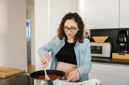 Photo for Horizontal photo with copy space of a domestic scene of a pregnant woman in casual clothes cooking at home. family and home concept - Royalty Free Image