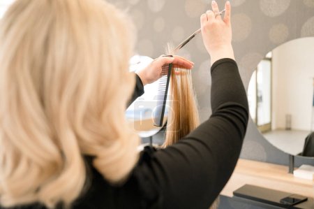 Téléchargez les photos : Gros plan de coiffeur méconnaissable coupant les cheveux blonds des femmes dans le salon de beauté. concept beauté et soins - en image libre de droit