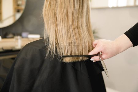 Foto de Vista posterior de la mujer irreconocible con el pelo rubio conseguir un corte de pelo por el estilista moderno - Imagen libre de derechos