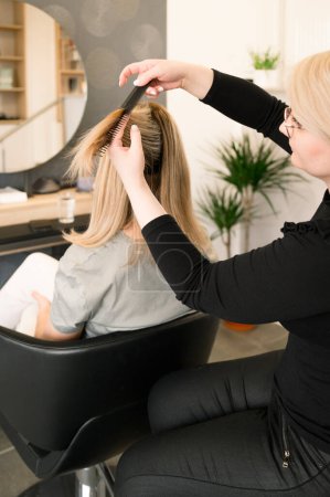 Téléchargez les photos : Vue arrière du coiffeur brossant et coupant les cheveux des clients, les femmes portant des vêtements décontractés. concept beauté et soins capillaires - en image libre de droit