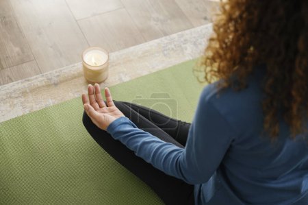 Photo for Back view of woman sitting crossed legs on mat, with candle light, meditating. daily morning routine. health and sporty lifestyle concept - Royalty Free Image