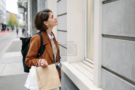 Foto de Mujer joven con bolsas de compras mirando un escaparate en la ciudad - Imagen libre de derechos