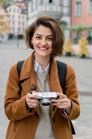 Vertikale Nahaufnahme einer jungen Straßenfotografin, die in der Stadt in die Kamera lächelt
