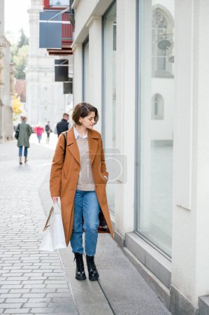 Téléchargez les photos : Photo verticale d'une femme marchant le long d'une rue commerciale lors d'une journée shopping en ville en hiver - en image libre de droit