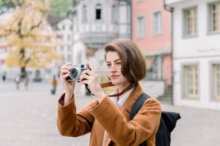 Porträt mit selektivem Fokus auf eine elegante junge Frau mit einer Kamera, die Fotos von einem Besuch in einer Stadt macht
