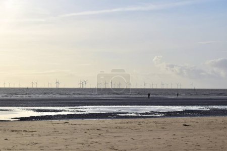 Téléchargez les photos : Journée claire avec des moulins à vent lointains et des hommes en fonte à Crosby Beach, Liverpool - en image libre de droit