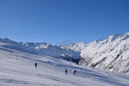 Skifahrer und Snowboarder im Skigebiet Hochgurgl, im Hintergrund das Otztal und die schneebedeckten Berge in Tirol, Österreich an einem schönen sonnigen Tag, perfekte Bedingungen für den Wintersport.