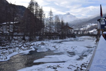 Beautiful view of a frozen river flowing through the Otztal Valley in Solden Alpine resort. The traditional Austrian town of Solden during the peak ski season in the winter months. Mountain backdrop.