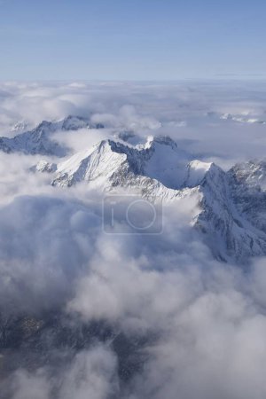 Breathtaking aerial view of alpine snowcapped mountain range peaking through heavy clouds. Mountain peaks of the Otztal Alps from above. The impressive winter view is taken from an airplane window.