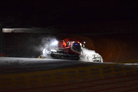 Téléchargez les photos : Un batteur de pistes travaillant au compactage de la neige dans une station de ski la nuit. - en image libre de droit