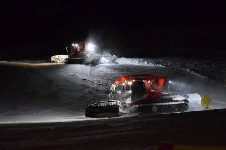 Téléchargez les photos : Deux bashers de pistes travaillant au compactage de la neige dans une station de ski la nuit. - en image libre de droit