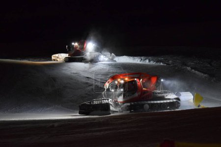 Téléchargez les photos : Deux bashers de pistes travaillant au compactage de la neige dans une station de ski la nuit. - en image libre de droit