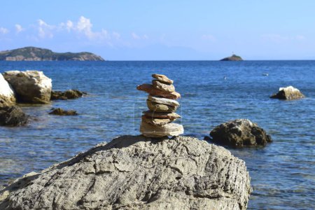 Montón equilibrado de rocas en una roca grande y áspera en una playa en la isla de Skiathos, Grecia. Retrocedido por el mar Egeo brillante y tranquilo y un cielo azul claro.