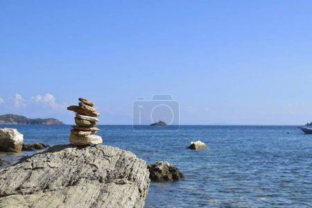 Foto de Montón equilibrado de rocas en una roca grande y áspera en una playa en la isla de Skiathos, Grecia. Retrocedido por el mar Egeo brillante y tranquilo y un cielo azul claro. - Imagen libre de derechos