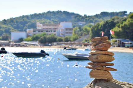Piedra balanceada en una roca grande y áspera en una playa en la isla de Skiathos, Grecia. Trasladado por barcos en el tranquilo mar Egeo, con un cielo azul claro y brillante.