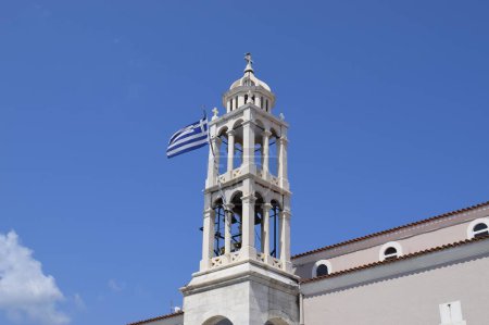 A Greek flag waving in the wind from the bell tower of a Greek Orthodox church (Cathedral of the Three Hierarchs) in Skiathos town, Greece.