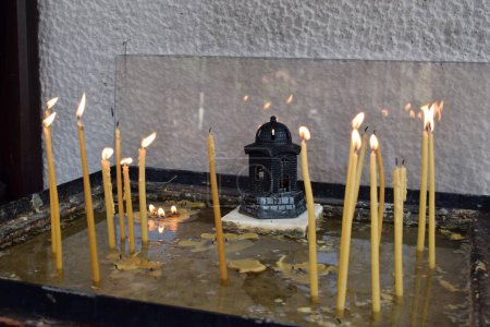 Burning candles in a small memorial outside a Greek Orthodox church in Skiathos town (Cathedral of the Three Hierarchs). Thin candles in a sandbox, Greece.