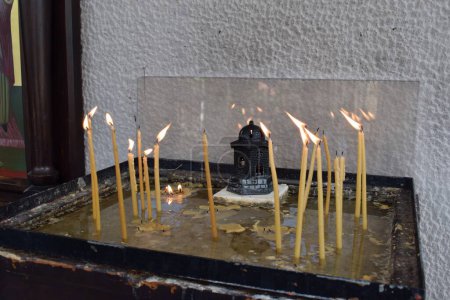 Burning candles in a small memorial outside a Greek Orthodox church in Skiathos town (Cathedral of the Three Hierarchs). Thin candles in a sandbox, Greece.