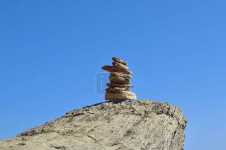 Montón bien equilibrado de rocas en una roca grande y áspera a lo largo de la costa griega, con un cielo azul claro y brillante.