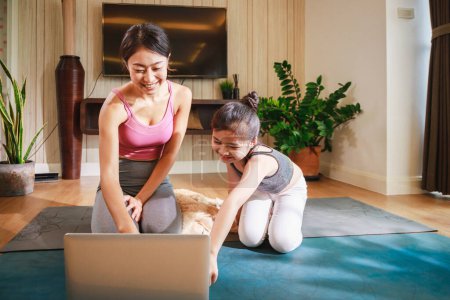Photo for Asian woman and daughter practicing yoga from yoga online course via laptop at living hom - Royalty Free Image