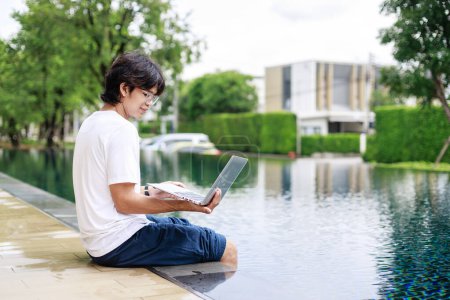 Téléchargez les photos : Travail d'ordinateur portable au bord de la piscine pour l'homme d'affaires en vacances dans l'usure occasionnelle - en image libre de droit