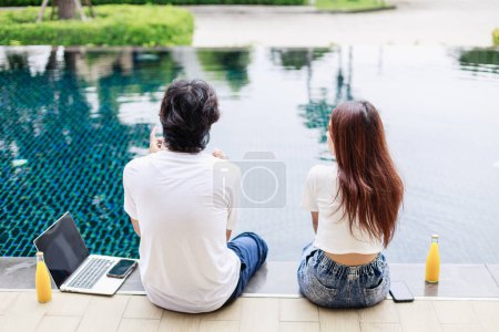 Téléchargez les photos : Heureux couple de gens d'affaires travaillant ensemble au bord de la piscine pendant les vacances à la maison - en image libre de droit
