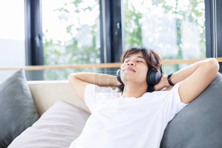Téléchargez les photos : Gros plan de l'homme écouter de la musique sur un canapé confortable à la maison. Temps de détente et de loisirs - en image libre de droit