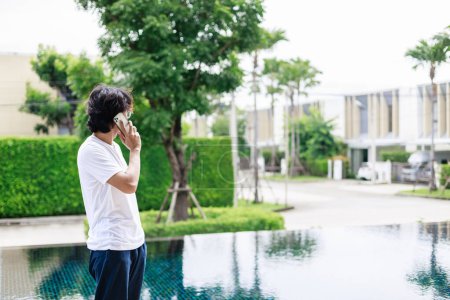 Téléchargez les photos : Un homme travaille à distance pendant les vacances et utilise un smartphone près de la piscine dans un hôtel de villégiature - en image libre de droit