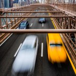 Moving taxi and other cars on Brooklyn bridge, the downtown of New York City in the background.