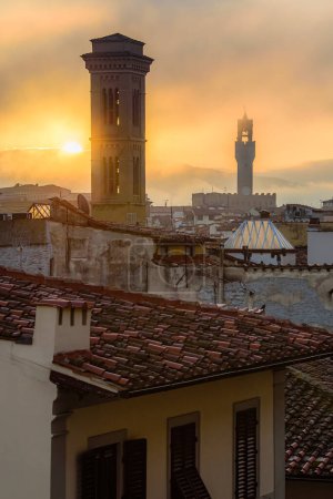 Foto de El sol naciente sobre el paisaje urbano de Florencia con las torres de la Chiesa di San Salvatore en Ognissanti y el Palazzo Vecchio en la mañana de otoño fogy. - Imagen libre de derechos