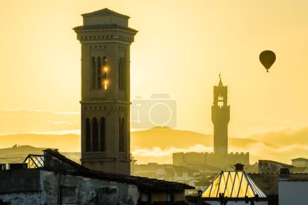 Foto de El sol naciente sobre el paisaje urbano de Florencia con las estrellas del sol en la torre de la Chiesa di San Salvatore en Ognissanti y el globo volador sobre el Palazzo Vecchio en la mañana de otoño. - Imagen libre de derechos