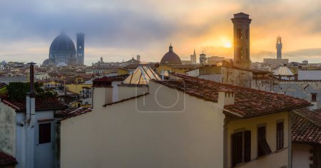 Foto de El sol naciente sobre el paisaje urbano de Florencia con las torres del Duomo, Chiesa di San Salvatore en Ognissanti y el Palazzo Vecchio en la mañana de otoño fogy. - Imagen libre de derechos