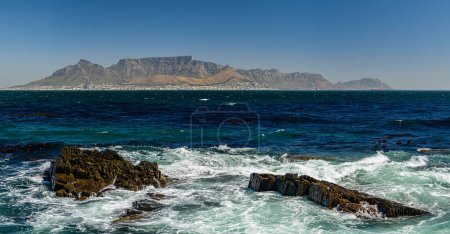 Foto de Montaña de la mesa en Ciudad del Cabo desde una distancia Robben Island. Acantilados rocosos en primer plano. - Imagen libre de derechos