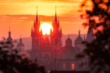 Die aufgehende Sonne zwischen den Türmen der Liebfrauenkirche vor Tyn in der UNESCO-Stätte Prag durch Blätter gesehen.