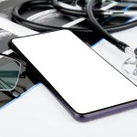 Smartphone with blank screen, MRI scan and stethoscope on white table